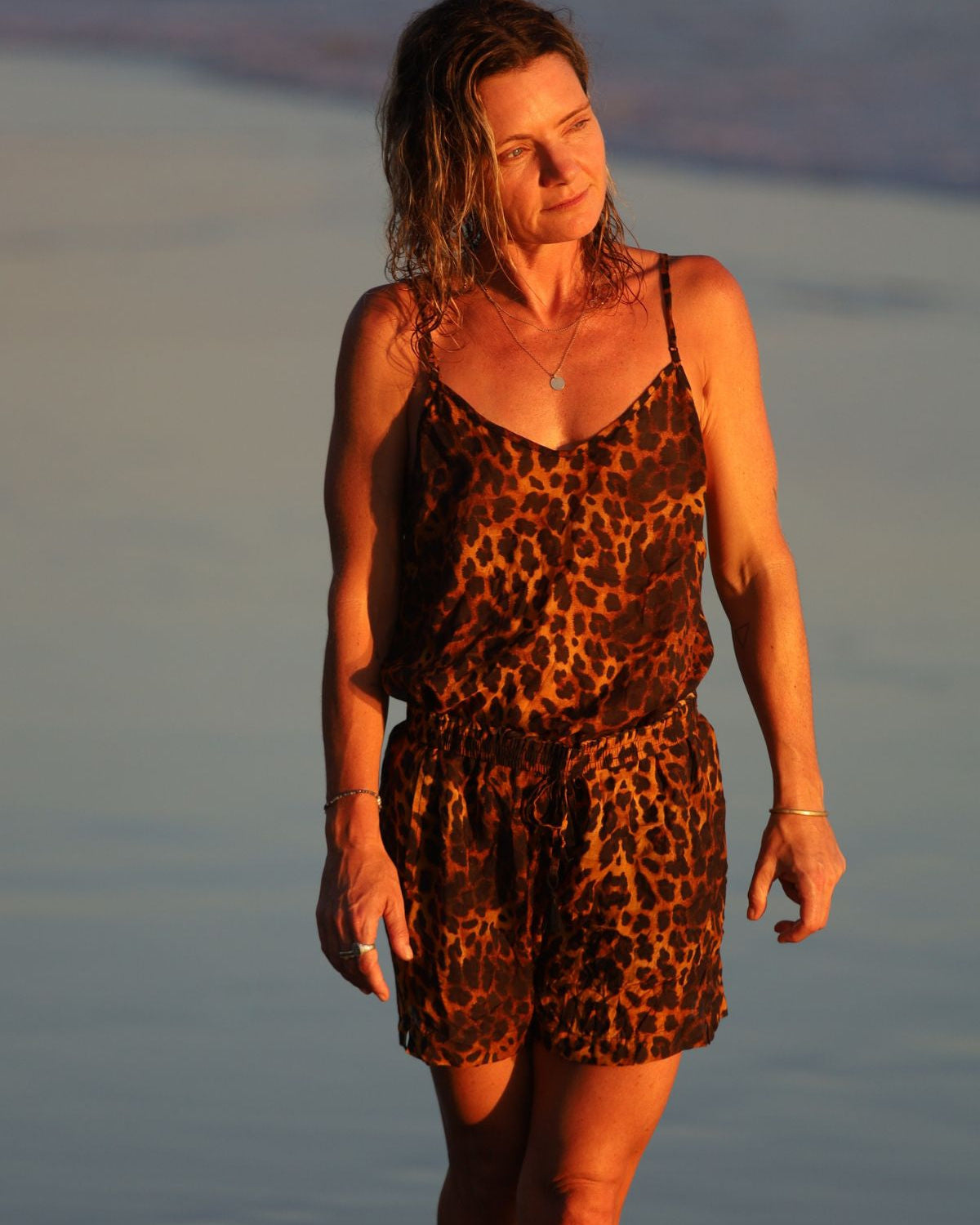 Woman in a leopard print dress standing on a beach at sunset.