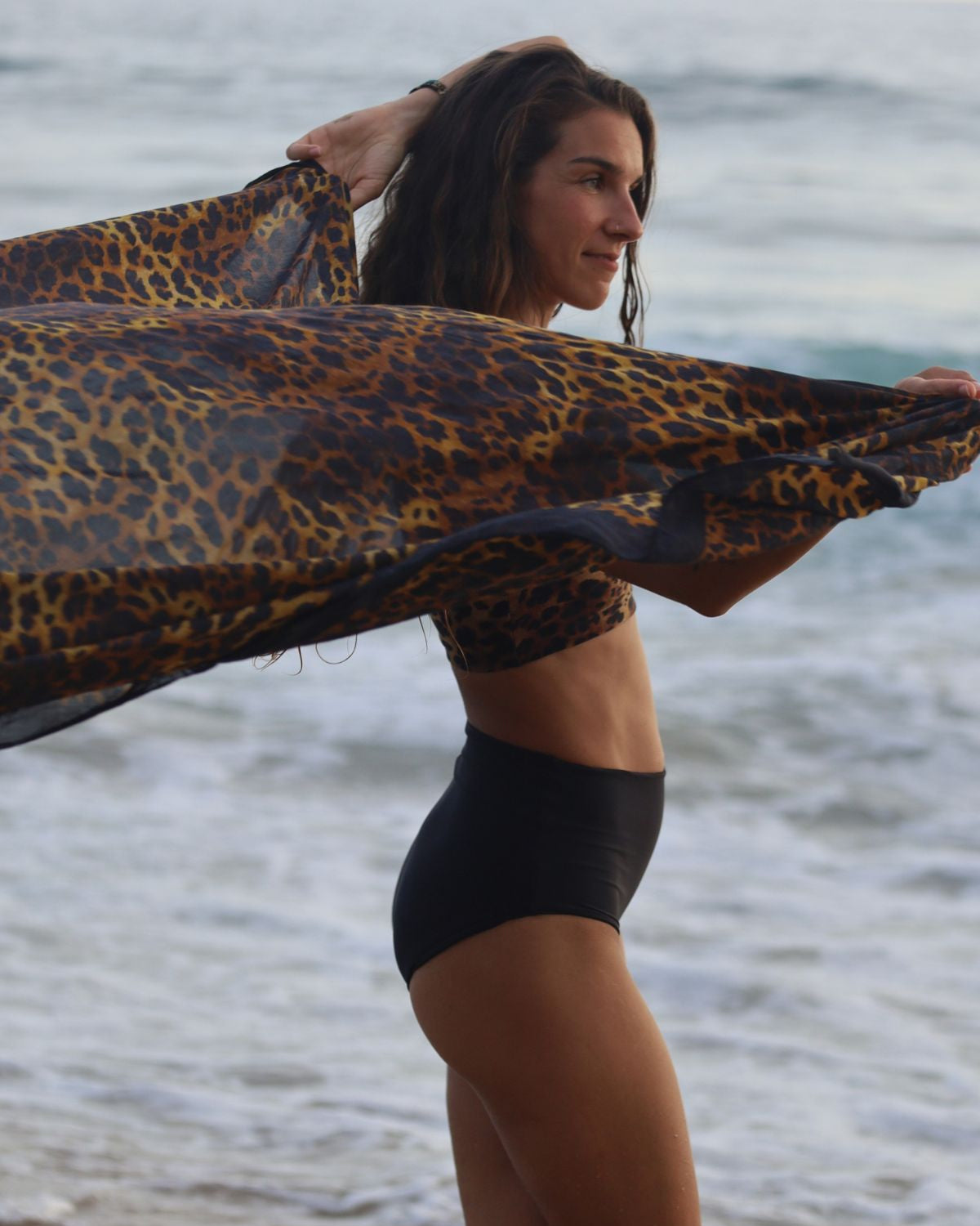 Woman holding a leopard-print surfboard against a beach background