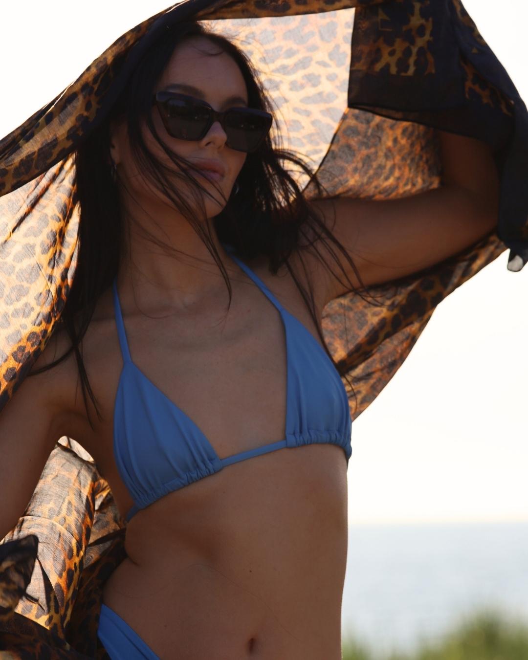 Woman in a blue bikini under a leopard print umbrella with a blurred natural background