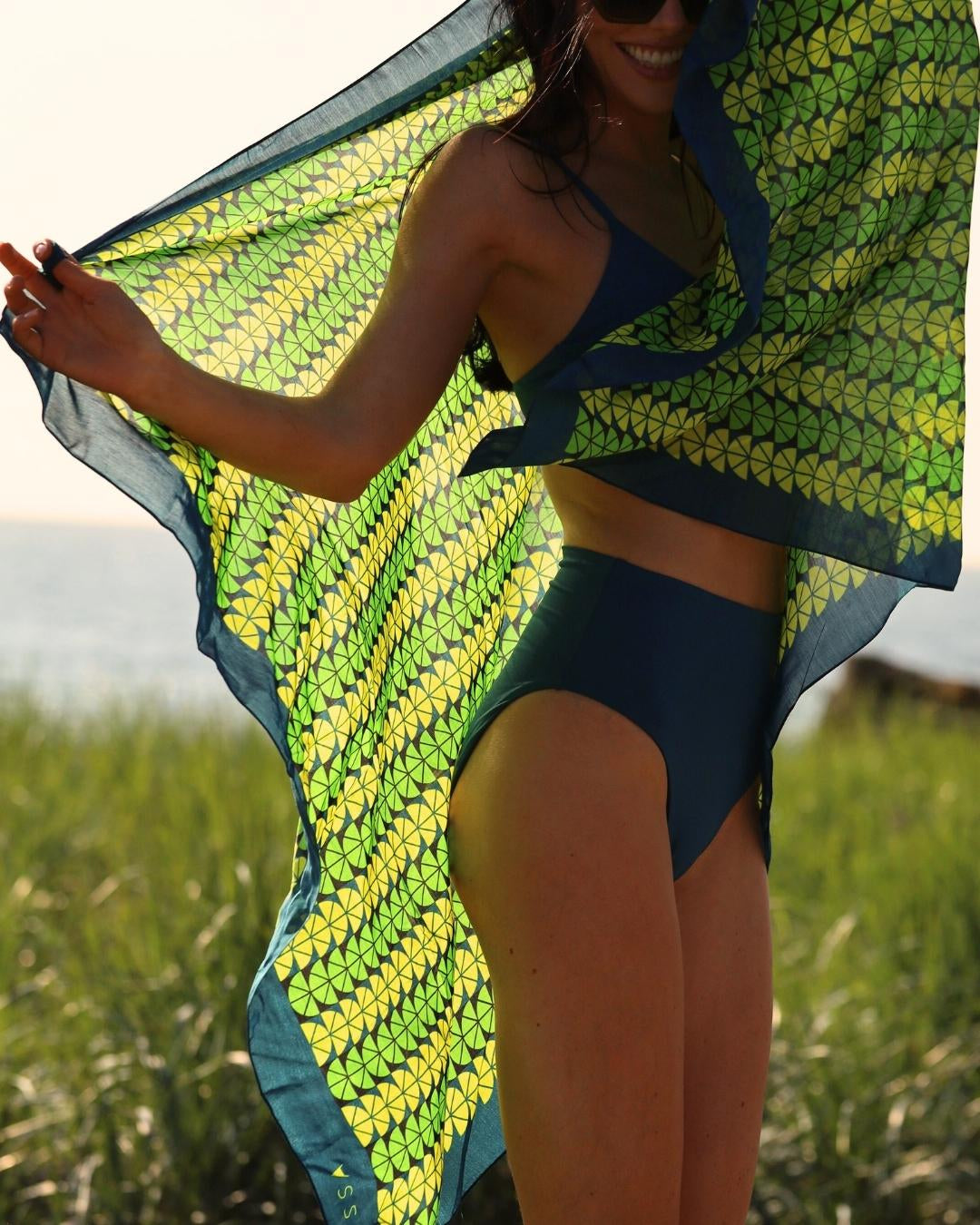 Woman in a blue bikini holding a green and yellow patterned towel outdoors.