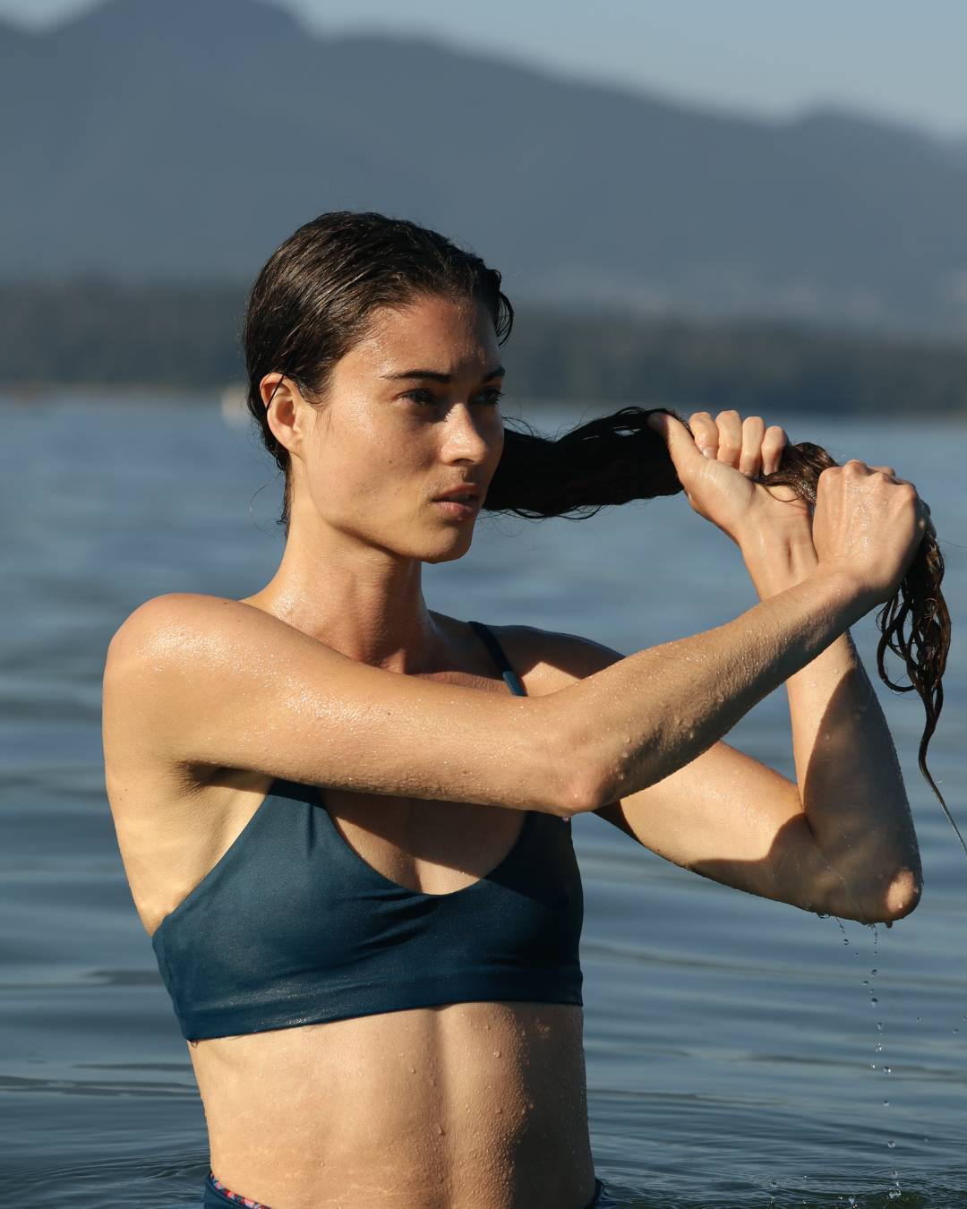 Person in a swimsuit standing in water with mountains in the background