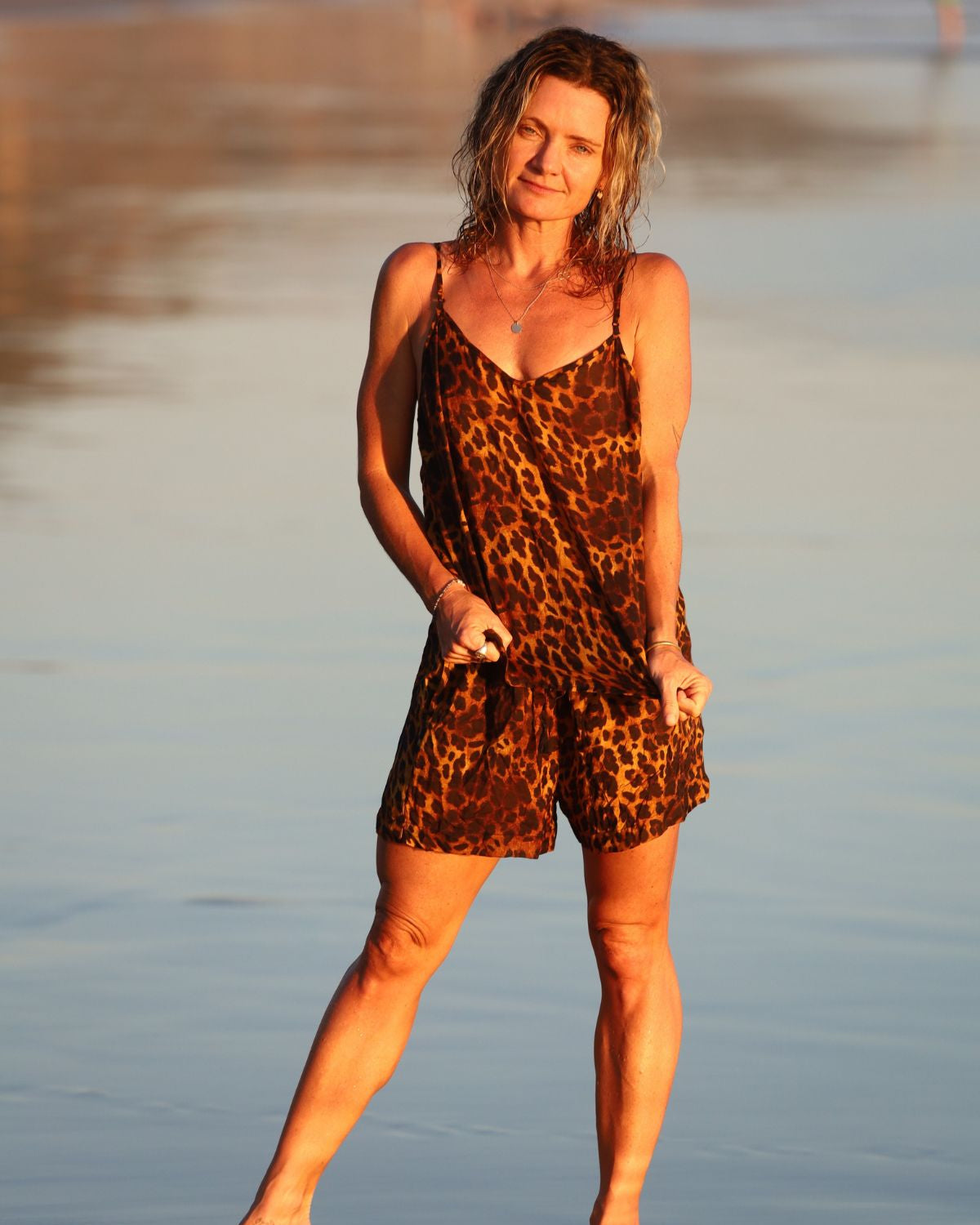 Woman in a leopard print dress standing on a beach at sunset.