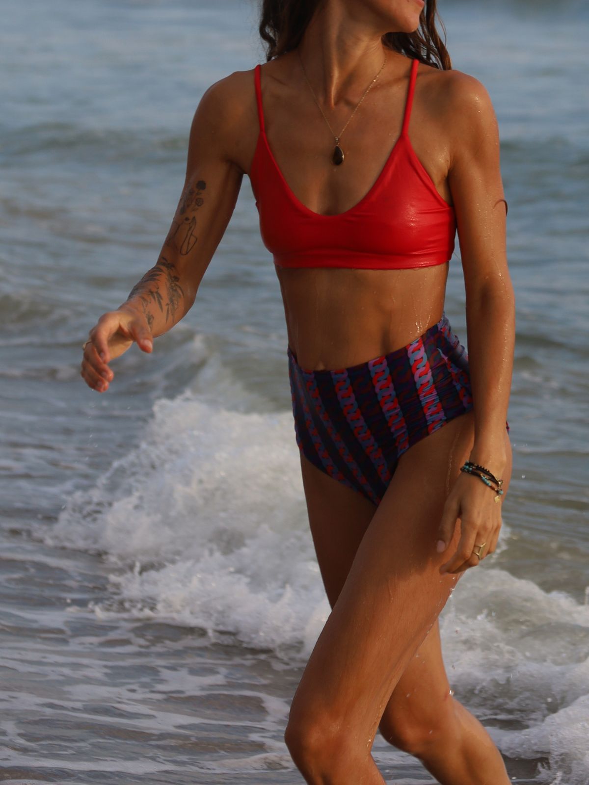 Person wearing a red bikini top and plaid shorts walking on a beach.