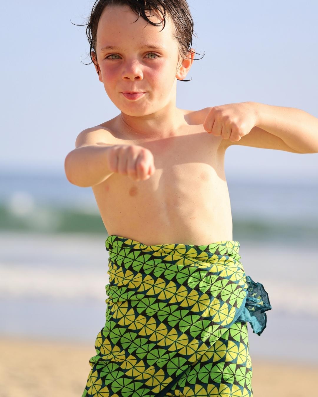 Child wearing a green and yellow patterned sarong on a beach